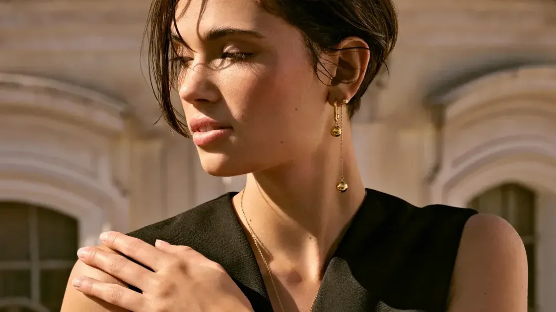 Woman in elegant black outfit wearing gold earrings and necklace from Beeline's fashion jewelry collection, showcasing the style of accessories distributed to 9,000+ retail locations