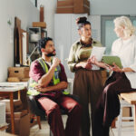 A small business team and a warehouse manager in a bright, compact fulfillment space discussing order volume and distribution strategy.