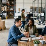 Four business professionals meeting at a table inside a warehouse facility, reviewing logistics data and discussing 3PL value-Added Services